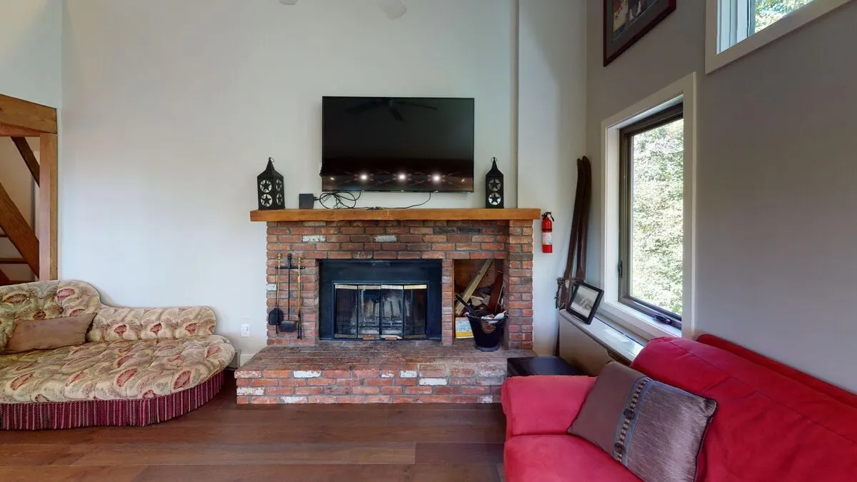 A stylish interior space featuring a fireplace, television, red couch, and a wooden staircase. The inviting setting is perfect for socializing, unwinding, or enjoying a friendly game night after skiing.