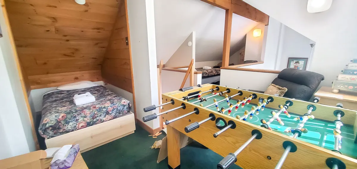 A foosball table takes center stage in this cozy loft space, accented by wooden details and a bed in the background. The scene conveys a sense of warmth and playfulness, ideal for relaxed evenings and spirited games.