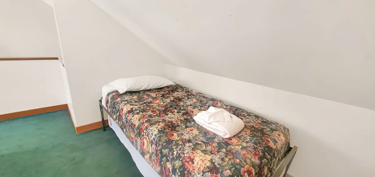 A welcoming bedroom featuring a bed with a floral blanket, crisp white pillow, and a neatly folded towel, creating an inviting atmosphere ideal for comfort and relaxation. The styling is cozy and thoughtful, suggesting a restful night's sleep or quiet moments shared.