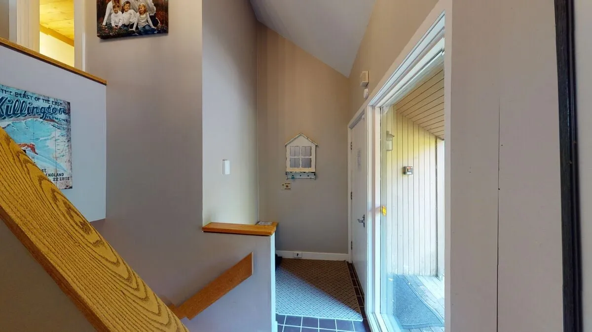 The image features the home's welcoming front entrance, with a view of the staircase just inside the door and curated wall decor hinting at a warm, inviting atmosphere. Natural light streams in, suggesting an easy transition from the outdoors to the comfort of home.