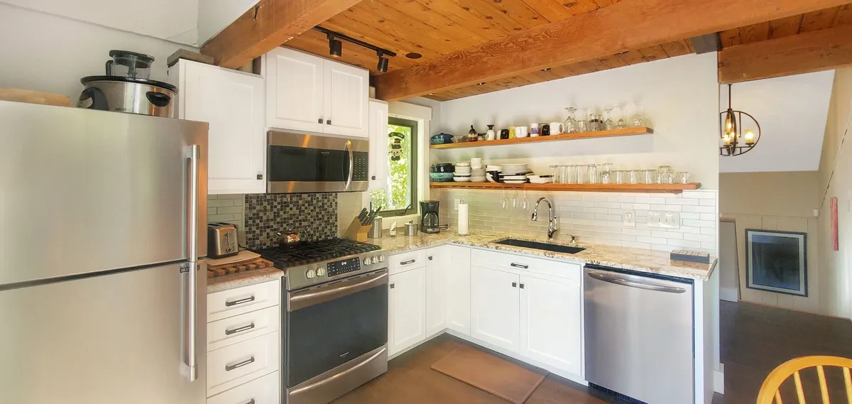 A bright kitchen area featuring stainless steel appliances, a broad granite countertop, and open shelving. Natural light streams in from a nearby window, creating an inviting atmosphere for entertaining or casual dining.