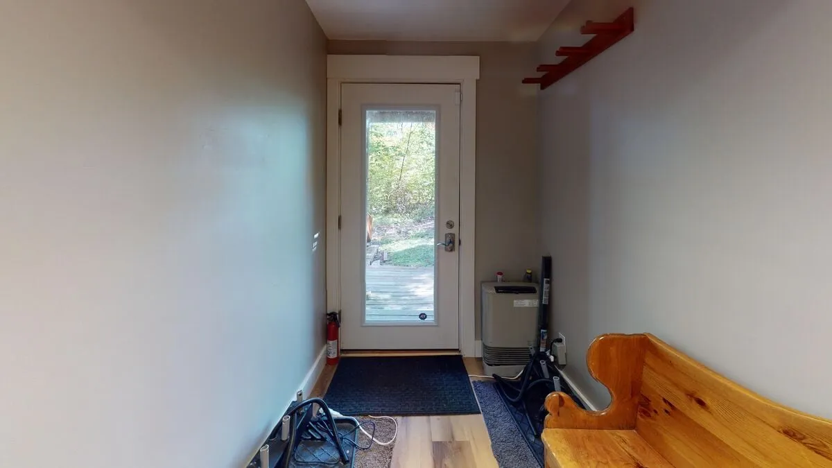 This image depicts the inviting front entryway of the lodge, featuring a wooden bench and doormat—an ideal spot for shedding boots and gear after a day skiing or snowboarding. The view transitions from the snowy outdoors to a cozy interior.