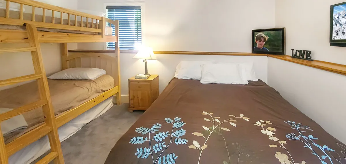A family-friendly bedroom with a bunk bed, double bed, nightstand with lamp, framed picture, and decorative 'LOVE' sign. The room is cozy and designed for family bonding, with elements that suggest comfort and togetherness.