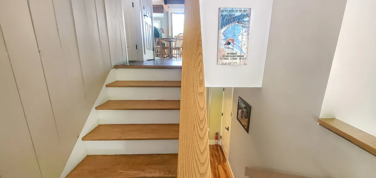 The image captures a staircase leading to an upper level, with wall art and a doorway visible, inviting viewers to imagine the transition to the fun-filled game loft above. Soft lighting and family photographs on the wall create a welcoming, homey atmosphere.