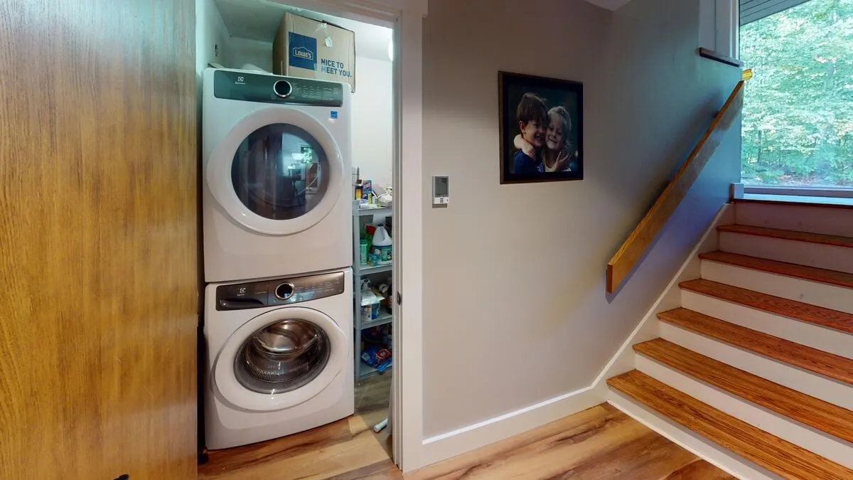 The scene captures a staircase leading upstairs, a stacked washer and dryer, and framed artwork, evoking the ease and practicality of home after a day outdoors. The space feels lived-in and accommodating, reinforcing the idea of family-friendly comfort.