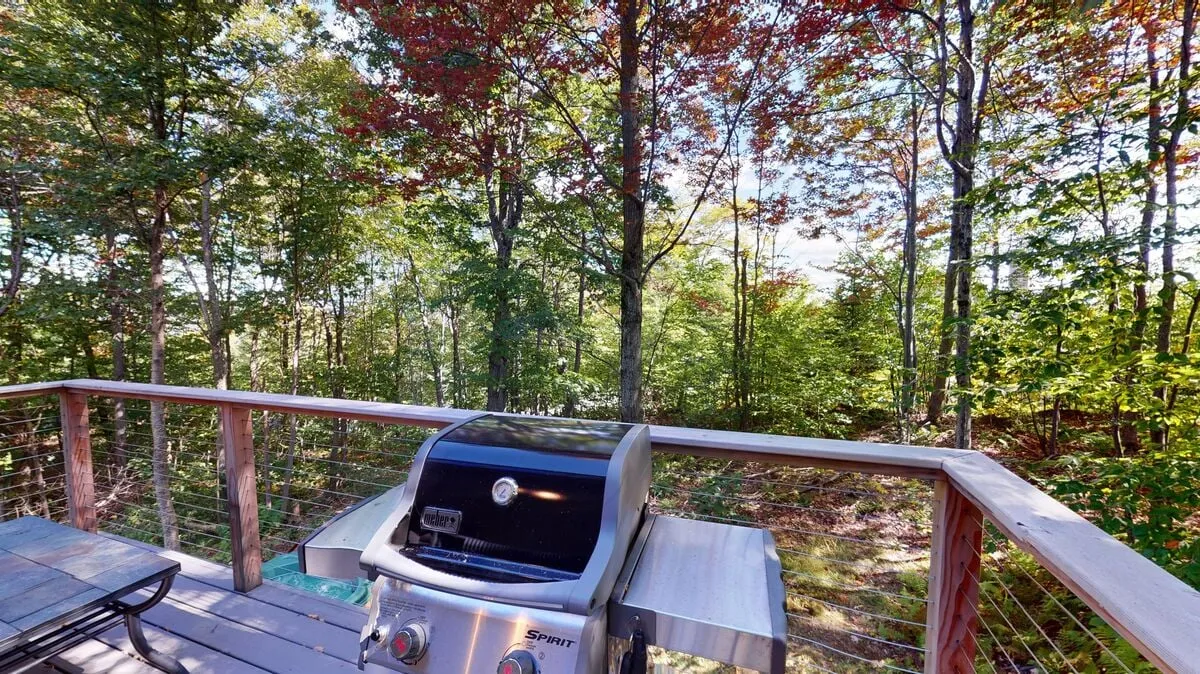 An inviting exterior shot featuring a grill setup on a wooden deck, complete with railings and surrounded by tall trees. The setting suggests an ideal place for outdoor gatherings, enjoying fresh air, and relaxing with friends or family after a day on the slopes.